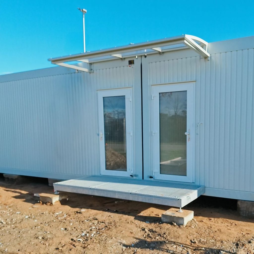 Aufnahme eines hellen Containergebäudes, das als Sozialunterkunft dient, von außen