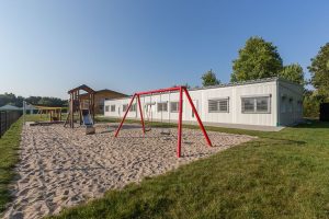Heller Kindertagesstättencontainer von außen mit einem Spielplatz im Vordergrund