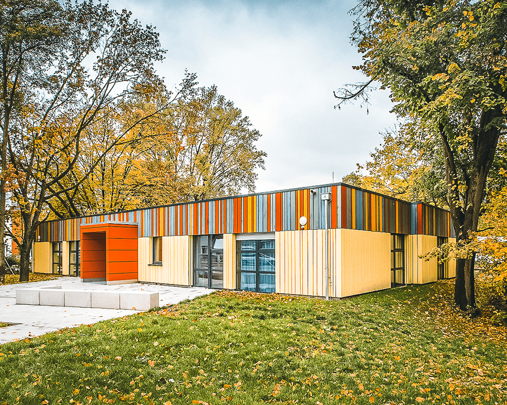 Aufnahme eines Container-Gebäudes einer Kindertagesstätte. Das Gebäude hat helle Wände und einen roten Türrahmen, der etwas hervorsteht.