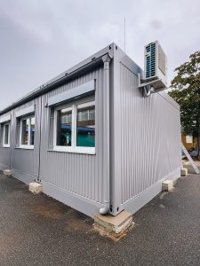Außenaufnahme eines silbergrauen Containergebäudes, welches als Erweiterung einer Schule in Beckum dient