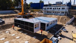 Kran hebt ein Containermodul der Flüchtlingswohnanlage von einem Tieflader