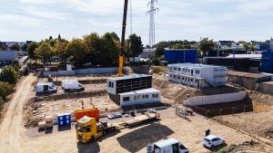 Kran hebt ein Containermodul der Flüchtlingswohnanlage von einem Tieflader