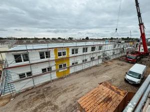 Aufnahme der Baustelle einer Wohnunterkunft für Flüchtlinge, mit einem roten Kranfahrzeug und einem weißen Kastenwagen