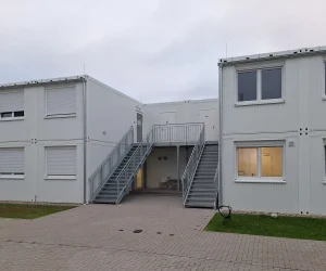 Außenansicht einer Flüchtlingsunterkunft bestehend aus mehreren weißen Modulen mit einer Treppe dazwischen