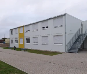Außenansicht einer Flüchtlingsunterkunft bestehend aus mehreren weißen Modulen mit farbigen Akzenten