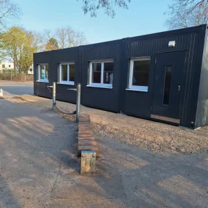 Außenansicht der anthrazitfarbenen Schulcontaineranlage in Schwalmtal mit einem Spielgerät davor